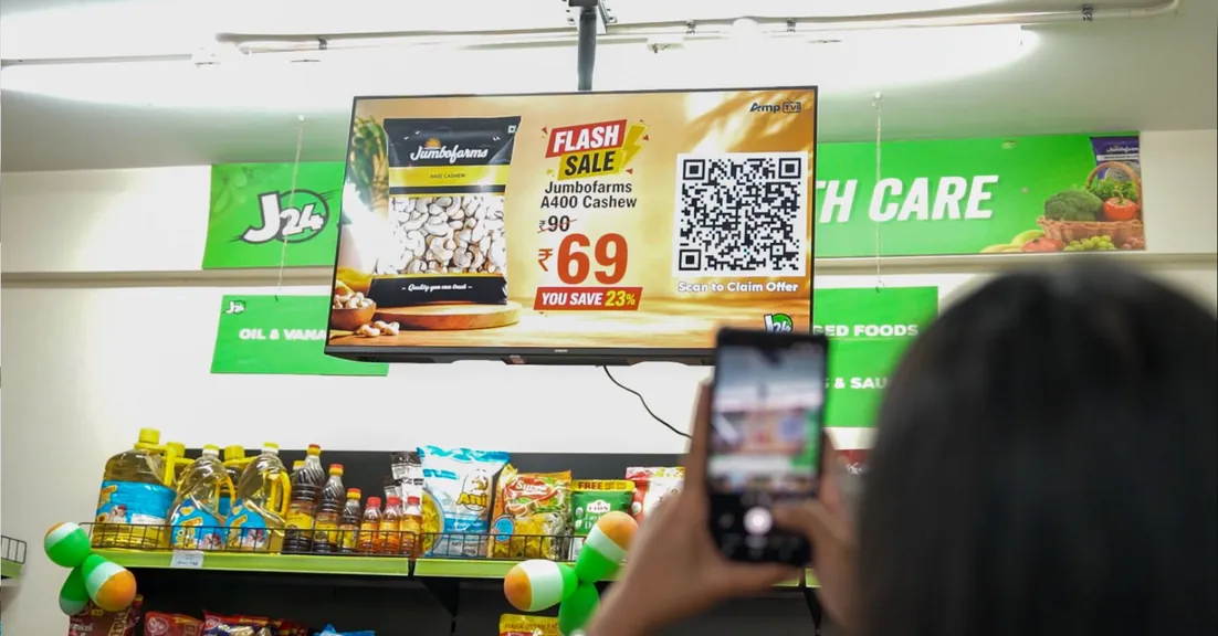 A customer scans a QR code on an Amp TV screen in a J24 store