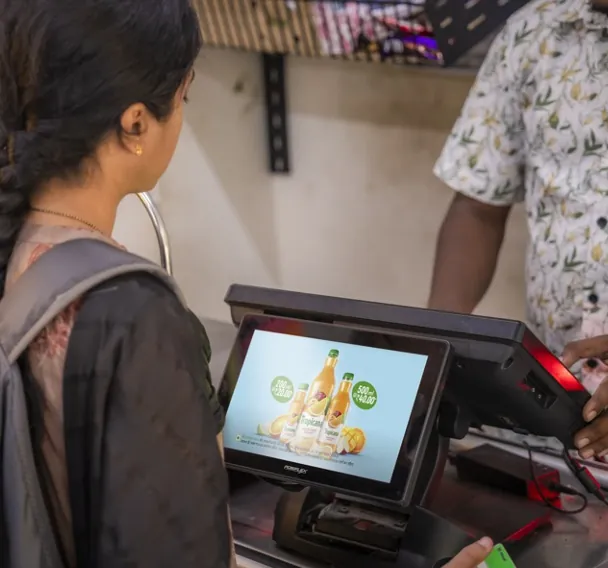 A customer at a J24 billing counter looks at a brand offer on the GoldenEye secondary screen